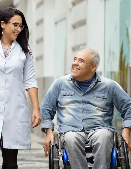 Carlos avanza en su silla de ruedas junto a una profesional de la salud. Ambos sonríen mientras disfrutan de un momento de alegría.